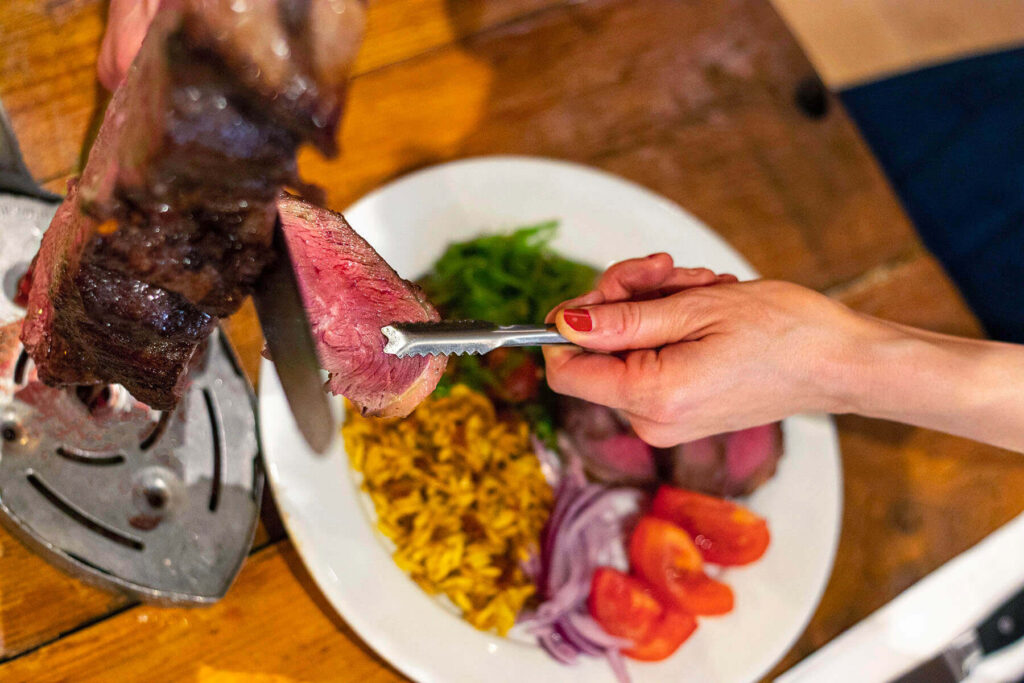 A person serving meat on a plate filled with colourful salad options.