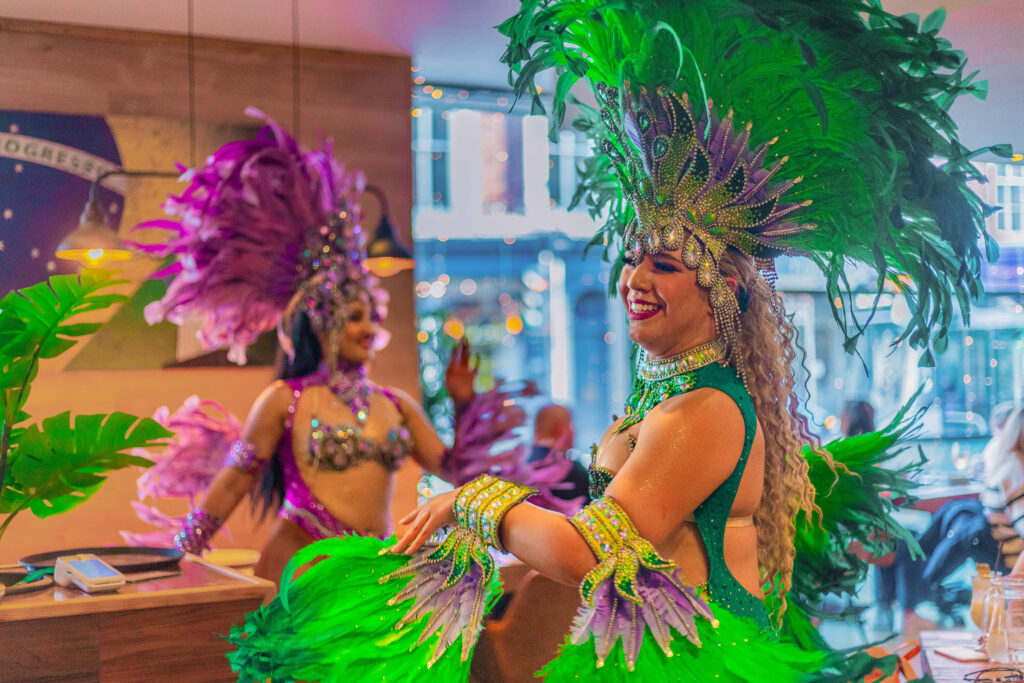 Brazilian samba dancers in vibrant green and purple feather costumes performing at Casa Brazilian Rodizio in York.