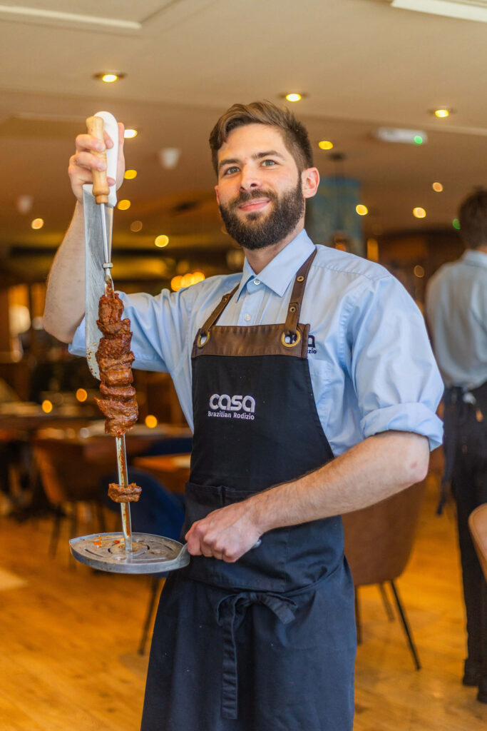 Casa Brazilian Rodizio waiter holding a skewer of grilled meat inside the restaurant in York.