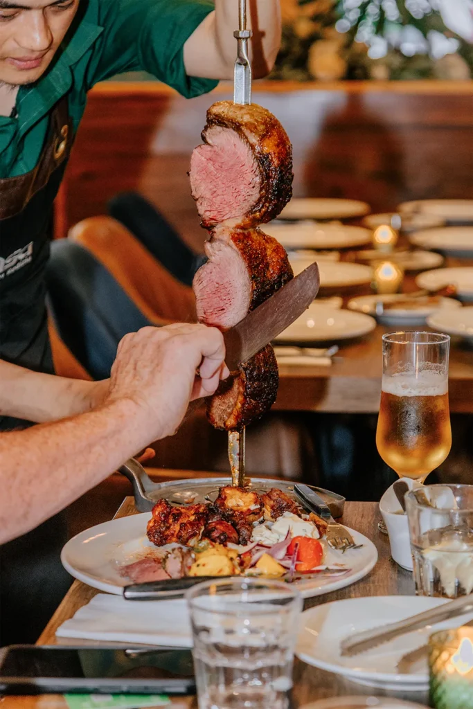 A server carves picanha steak with a browned crust and pink centre from a skewer at a guest’s table at Casa Brazilian Rodizio in York.